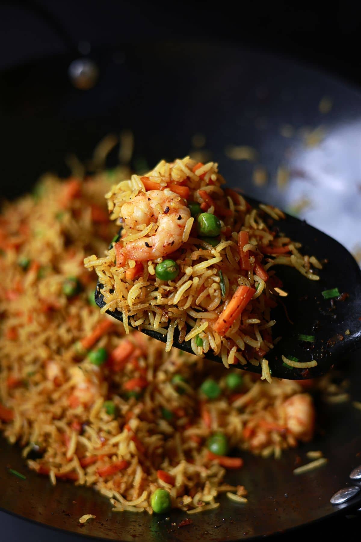 Curry fried rice is held on a spatula inside the wok.