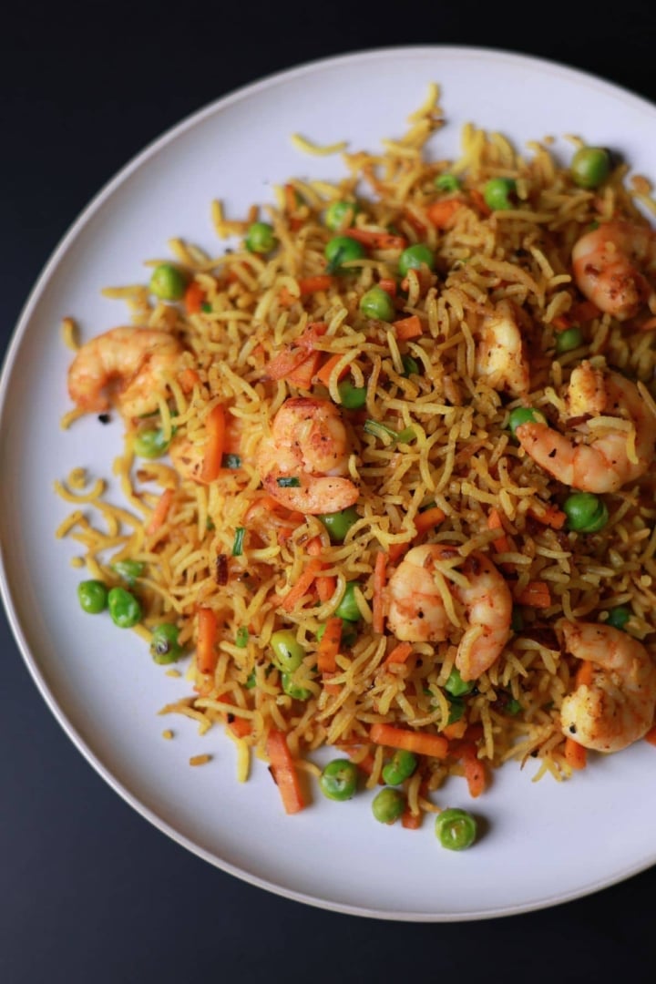 Curry fried rice with shrimp served on a white plate.