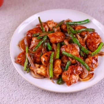 Close-up of juicy chicken and crisp green beans coated in stir fry sauce.