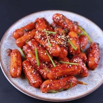 Close-up of spicy sausage stir fry served on a white plate with sesame seeds and green onion.