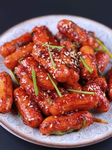 Close-up of spicy sausage stir fry served on a white plate with sesame seeds and green onion.