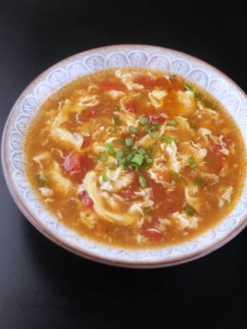 Tomato egg drop soup served in a bowl, garnished with green onions.