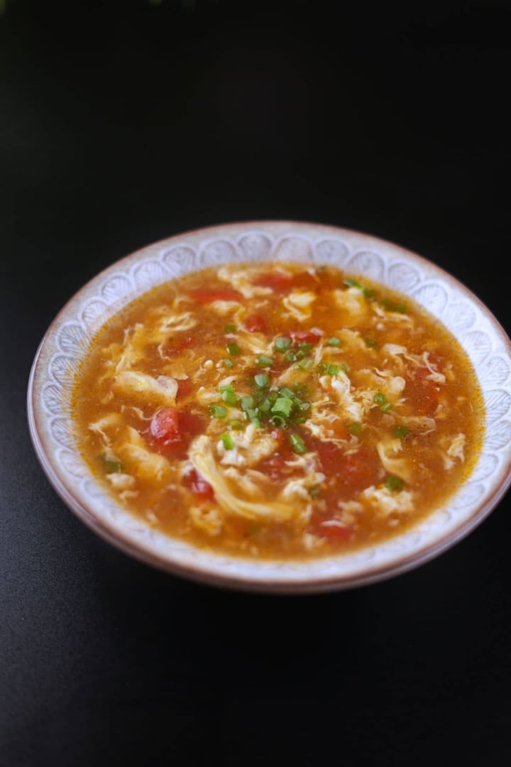Tomato egg drop soup served in a bowl, garnished with green onions.