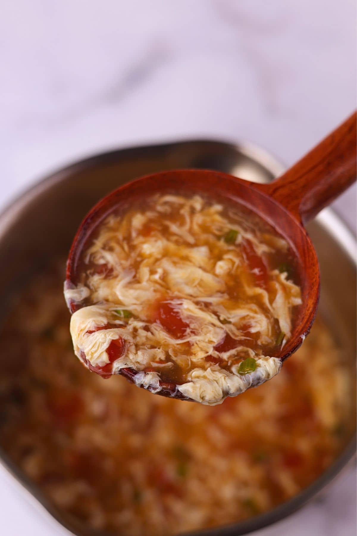 A ladle scooping up silky tomato egg drop soup with egg ribbons.