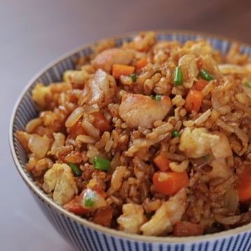 A bowl of hibachi chicken fried rice topped with green onions, served on a wooden table.