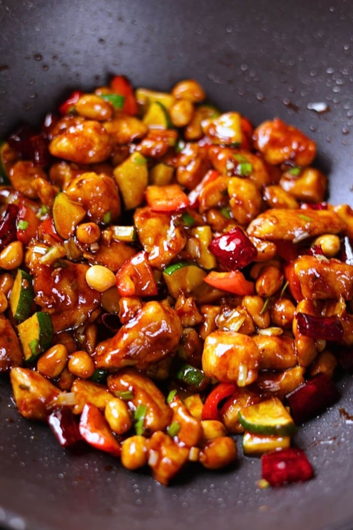 Close-up of Kung Pao Chicken showing tender chicken pieces, crunchy peanuts, and dried red chilies in a glossy sauce.