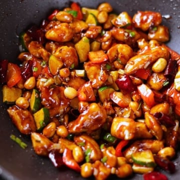 Kung pao chicken coated in a glossy sauce with veggies, peanuts, and dried red chilies.