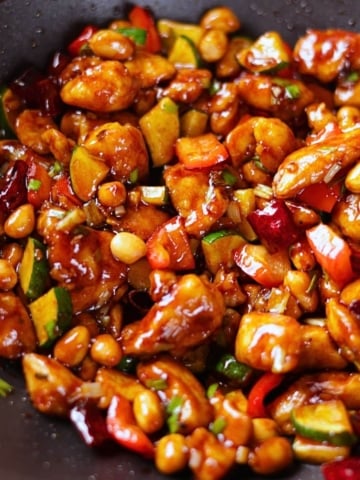 Kung pao chicken coated in a glossy sauce with veggies, peanuts, and dried red chilies.