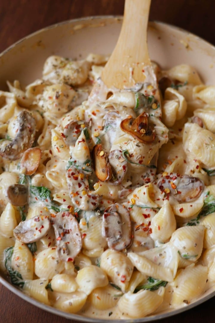 Creamy spinach and mushroom pasta in a off white pan.