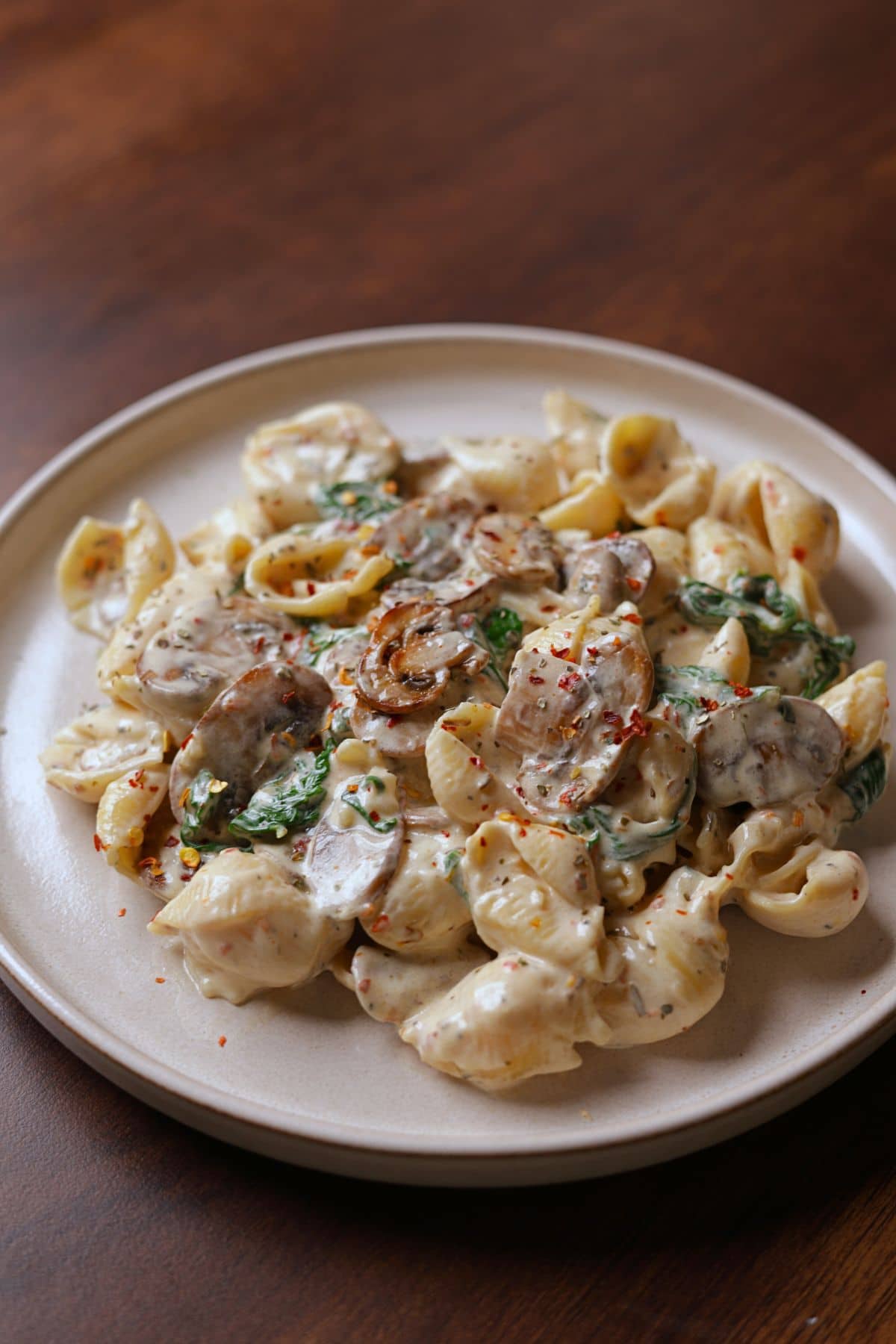 Creamy mushroom and spinach pasta served on a plate, topped with chili flakes.
