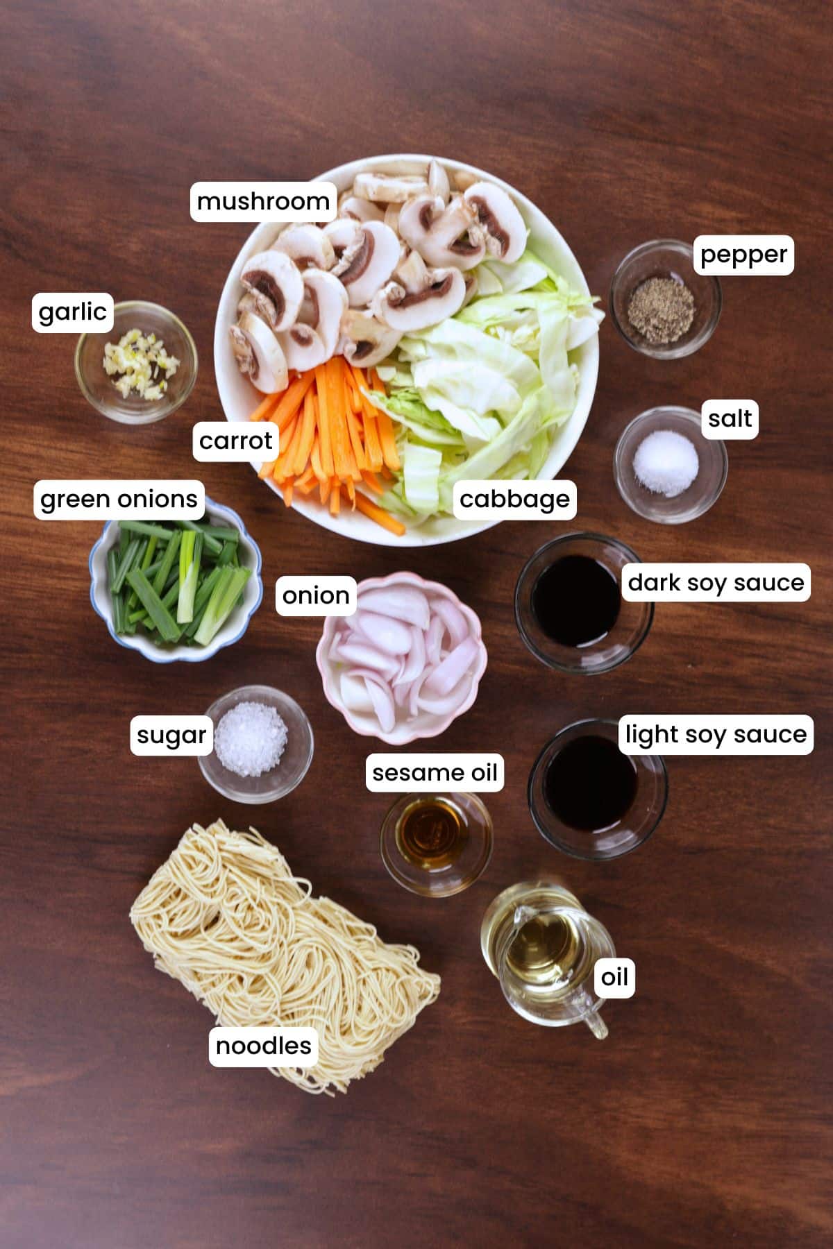 Fresh vegetables, noodles, and seasonings for chow mein on a wooden background.