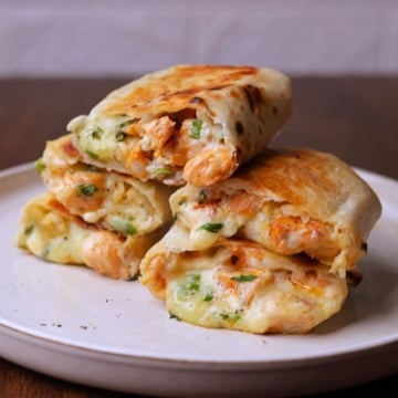 Stacked chicken wraps with melted cheese on a off white platter.