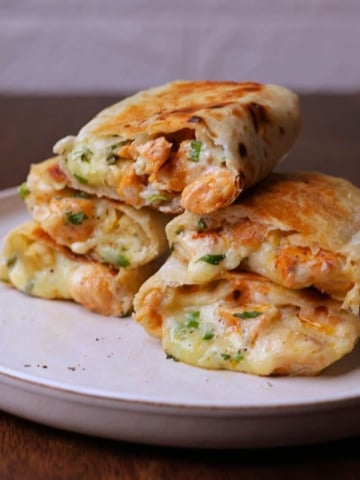 Stacked chicken wraps with melted cheese on a off white platter.