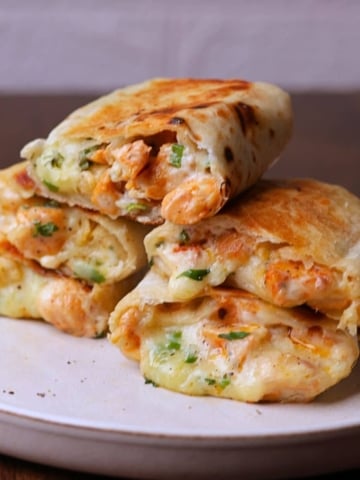 Stacked chicken wraps with melted cheese on a off white platter.