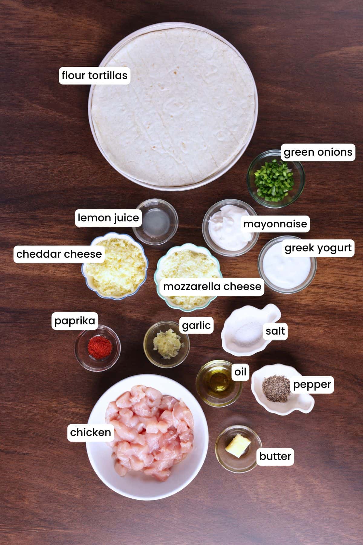 Flat lay of chicken, cheese, garlic, tortillas, and seasonings on a wooden surface.