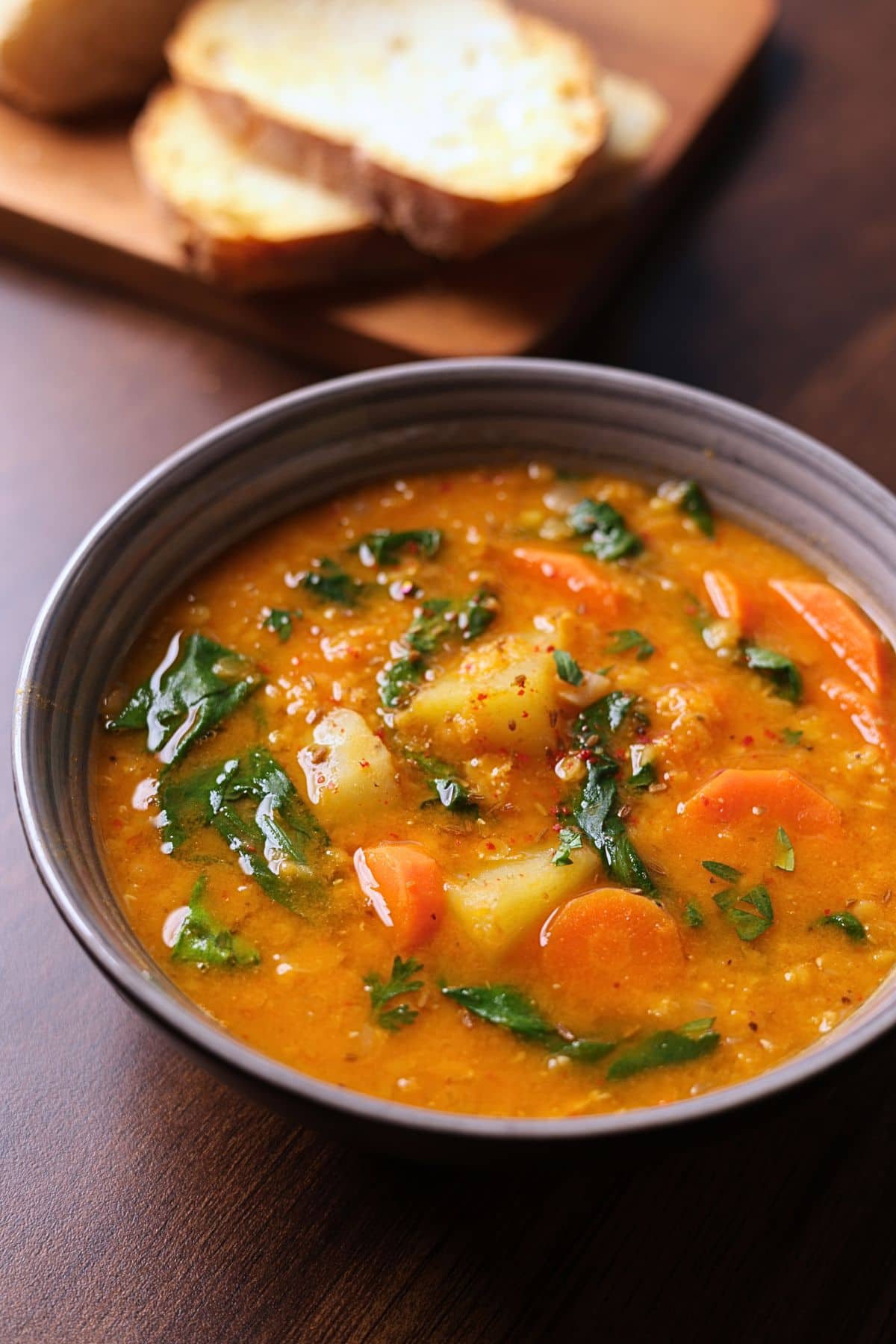 Bowl of red lentil and vegetable soup accompanied by slices of bread.
