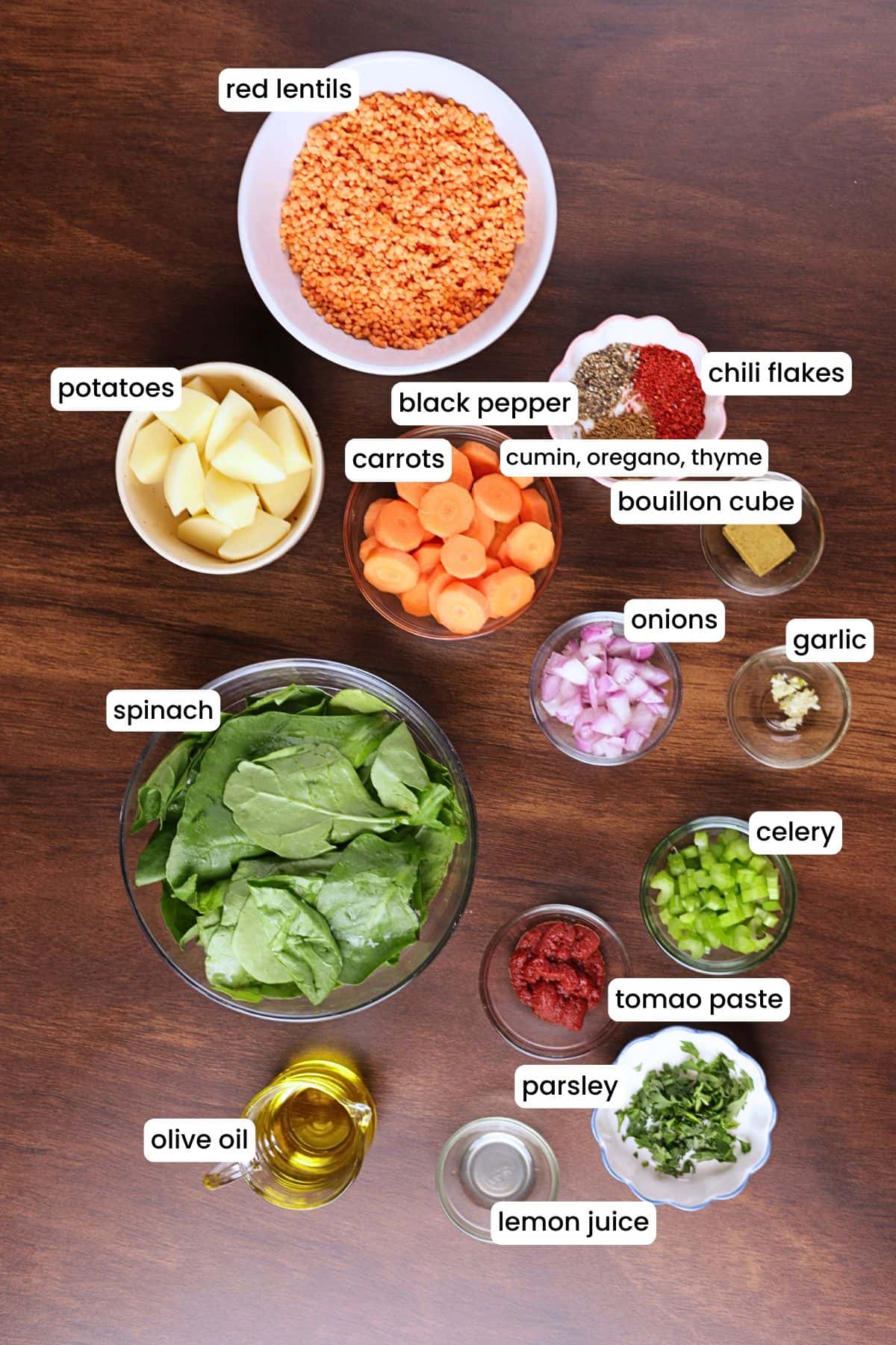 Ingredients for red lentil soup laid out on a wooden backdrop, including red lentils, carrots, celery, onion, garlic, and spices.