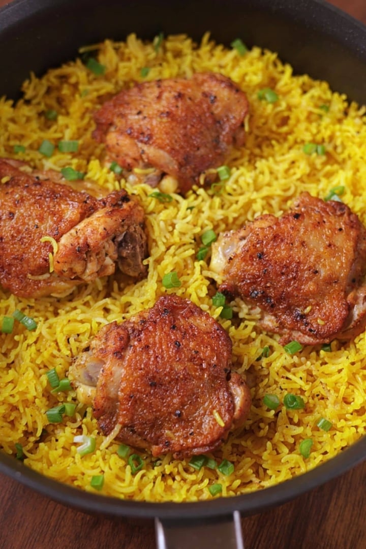 Easy one pan chicken and yellow rice with four chicken thighs in a skillet.