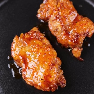 Crispy honey garlic chicken thighs served on a black platter with a glossy sticky glaze.