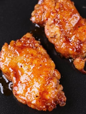 Crispy honey garlic chicken thighs served on a black platter with a glossy sticky glaze.