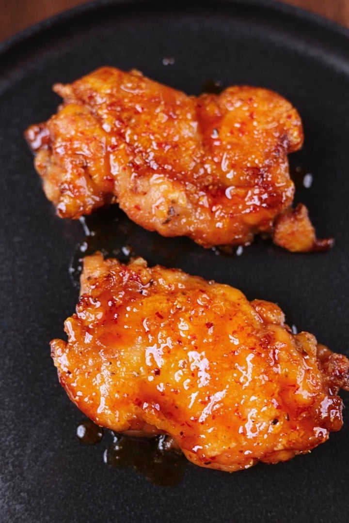 Crispy honey garlic chicken thighs served on a black platter with a glossy sticky glaze.