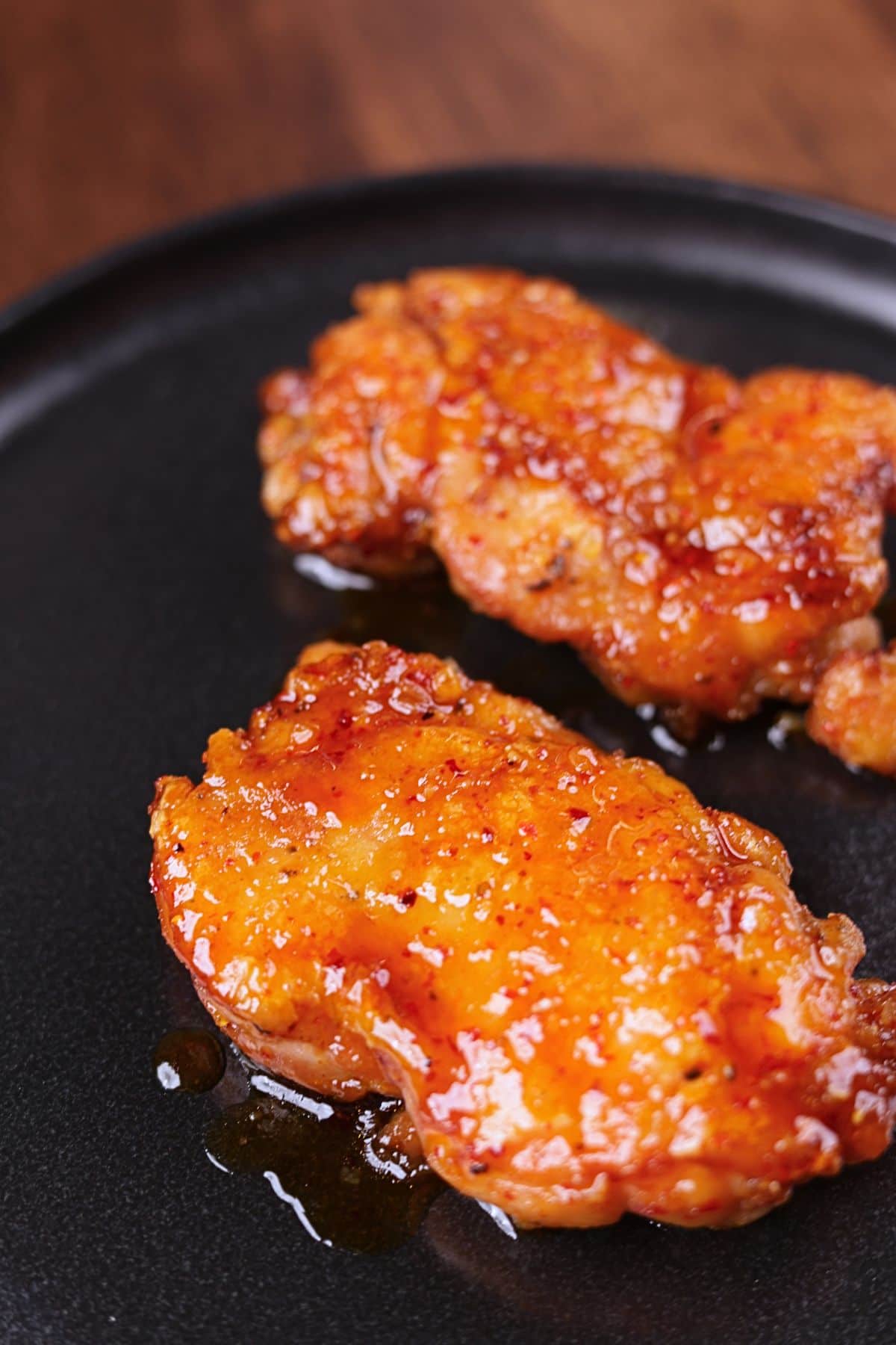 Crispy honey garlic chicken thighs served on a black platter with a glossy sticky glaze.