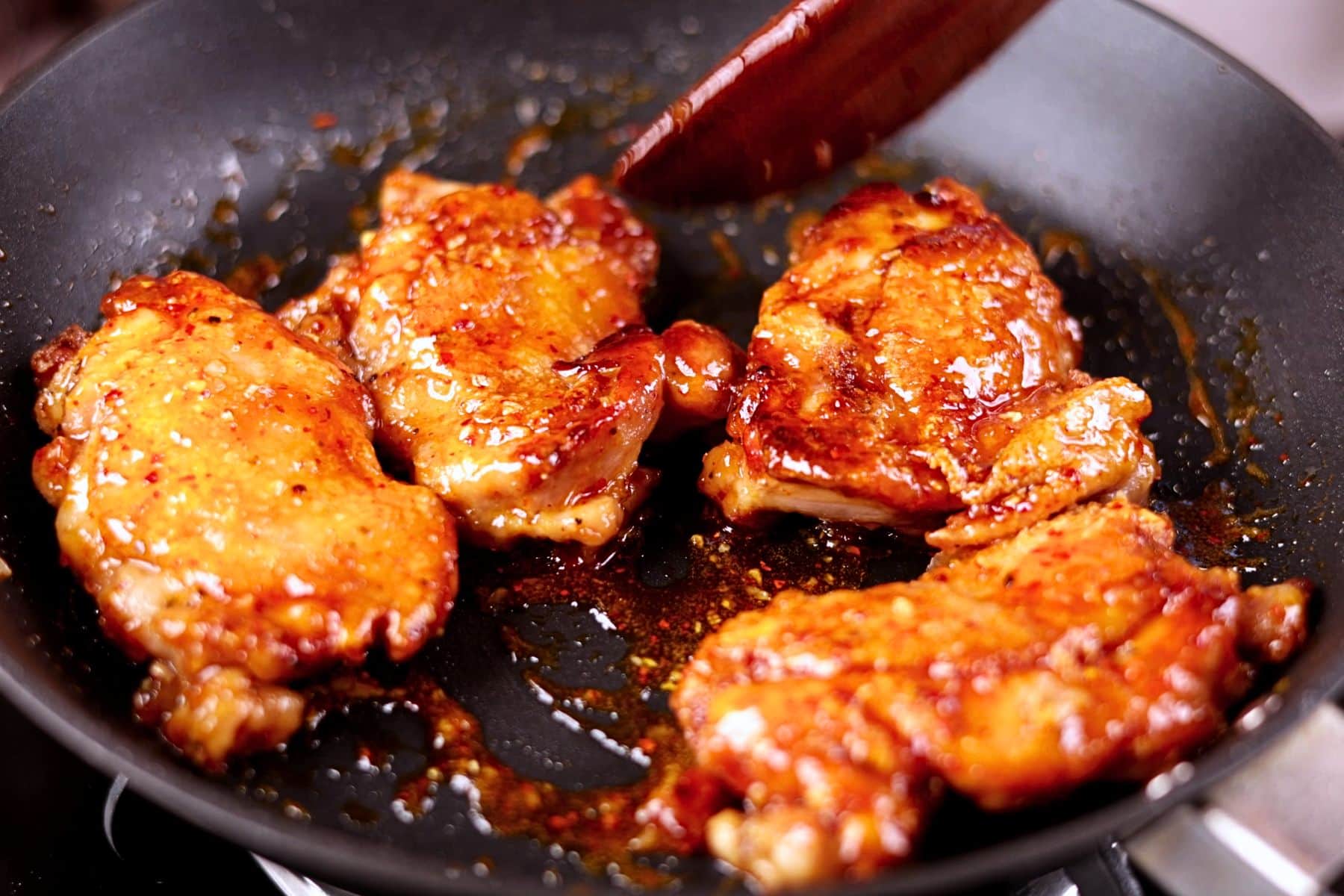 Tossing the crispy chicken thighs with the honey garlic sauce in the pan.