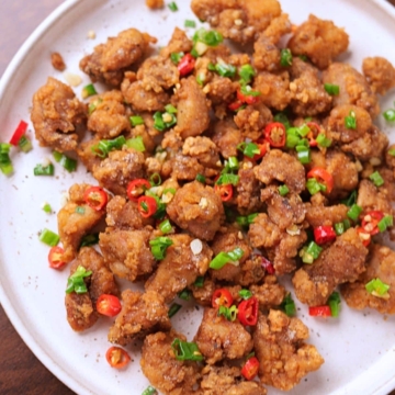 Crispy salt and pepper chicken served on a platter garnished with green onions and red chilies.