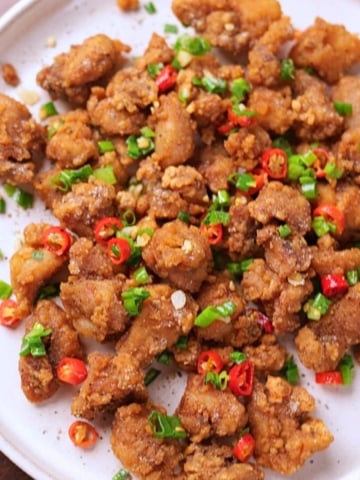Crispy salt and pepper chicken served on a platter garnished with green onions and red chilies.