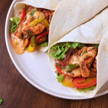 Chicken fajita wraps filled with seasoned chicken, bell peppers, onions, lettuce, and creamy sauce on a white platter.