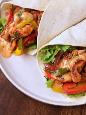 Chicken fajita wraps filled with seasoned chicken, bell peppers, onions, lettuce, and creamy sauce on a white platter.