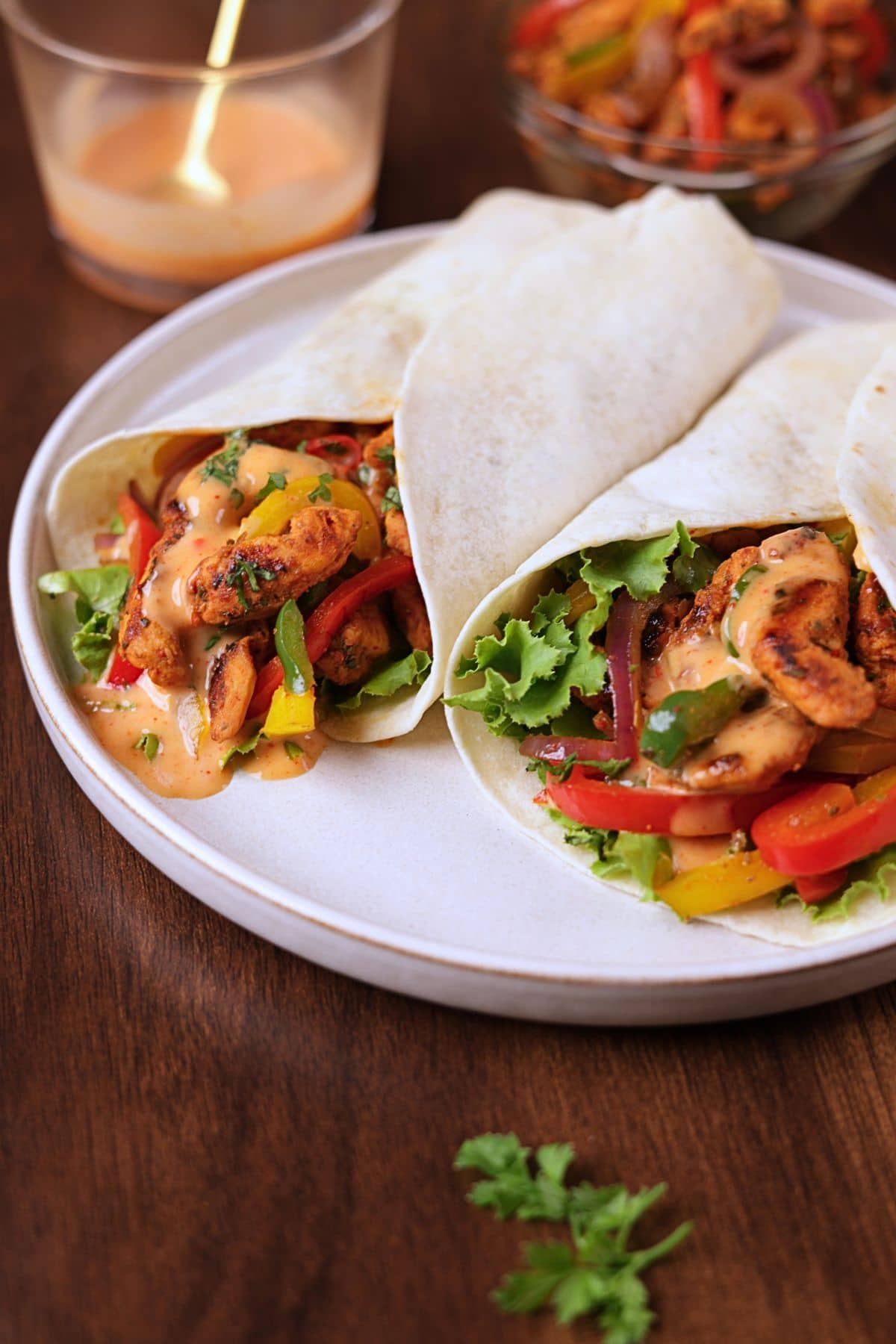 Fajita wraps filled with seasoned chicken, bell peppers, onions, lettuce, and creamy sauce on a white platter.