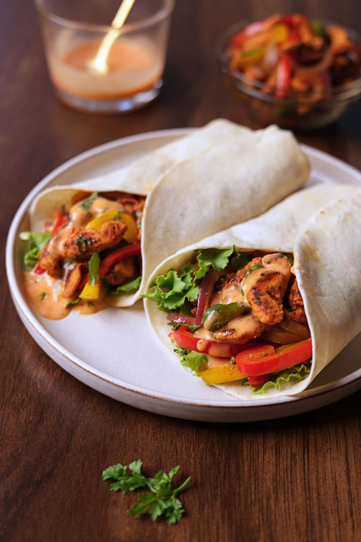 Chicken fajita wraps filled with seasoned chicken, bell peppers, onions, lettuce, and creamy sauce on a white platter.