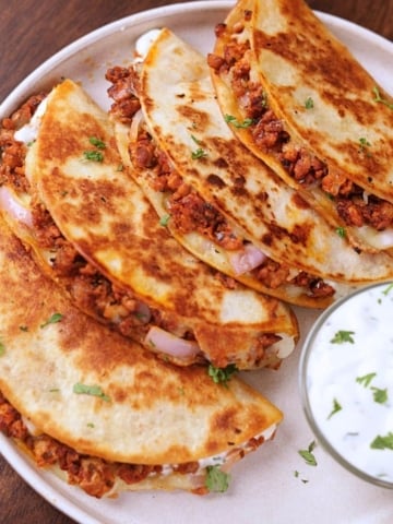 Crispy ground chicken tacos served on a white plate with creamy garlic sauce on the side.