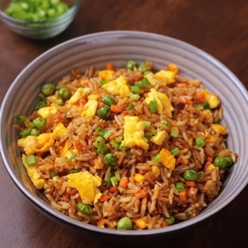 Egg fried rice served in a bowl with carrots, peas, eggs, and green onions.