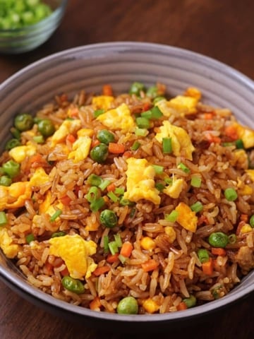 Egg fried rice served in a bowl with carrots, peas, eggs, and green onions.