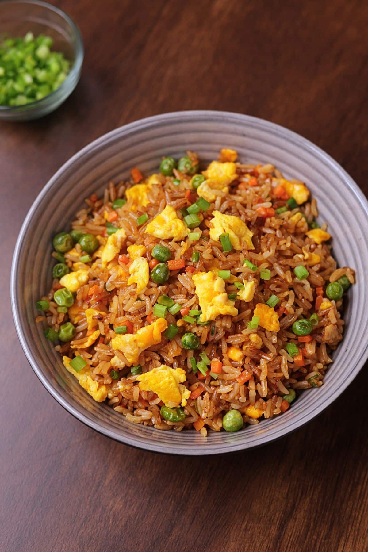 Egg fried rice served in a bowl with carrots, peas, eggs, and green onions.