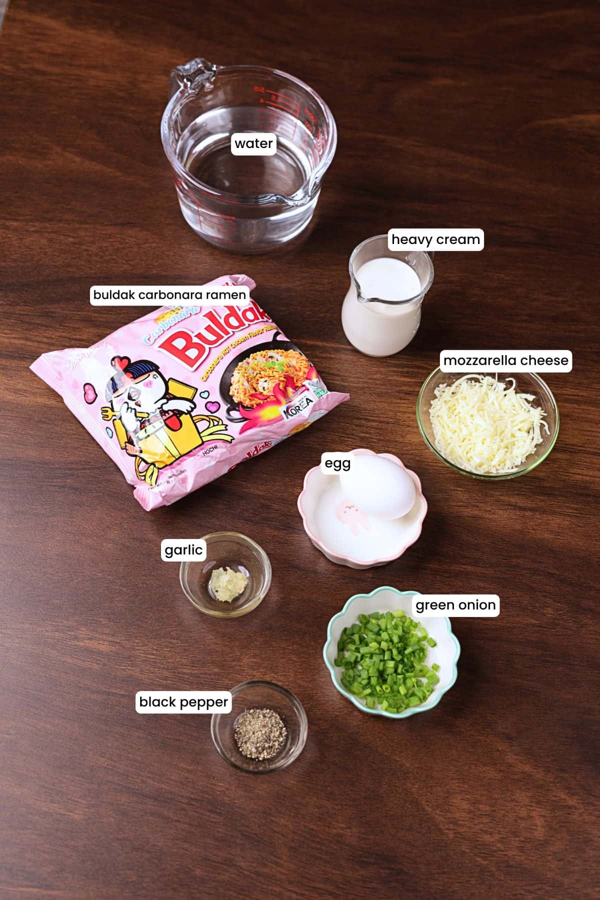 Ingredients for creamy Buldak ramen including Buldak Carbonara ramen, heavy cream, mozzarella cheese, egg, garlic, black pepper, and green onion.