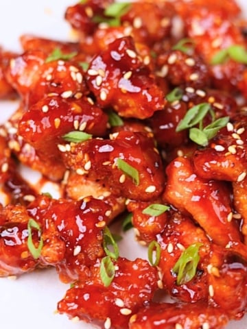 Gochujang chicken garnished with green onions and sesame seeds.