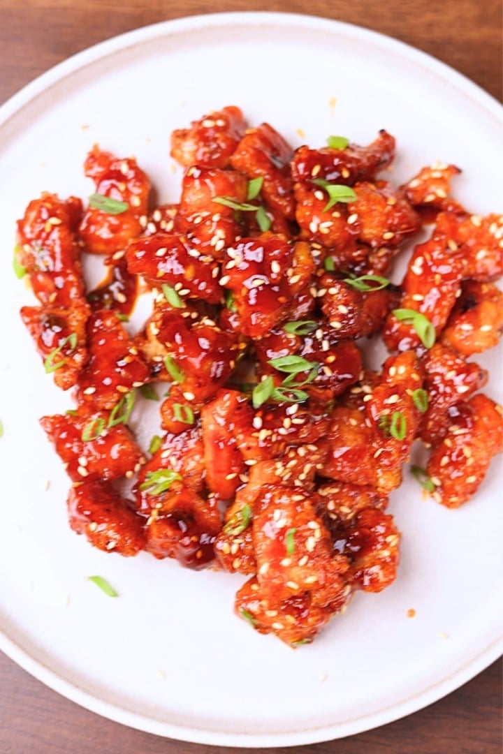 Sticky gochujang chicken garnished with green onions and sesame seeds.