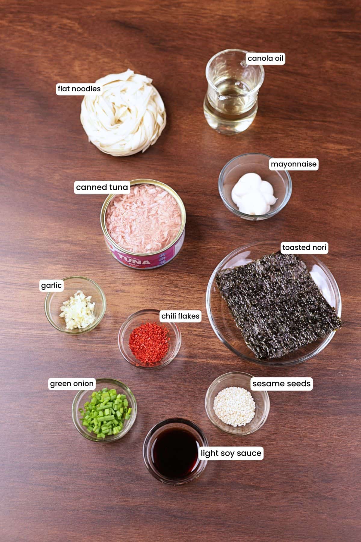 Ingredients for 15-minute tuna noodles including flat noodles, canned tuna, mayonnaise, soy sauce, garlic, chili flakes, sesame seeds, green onion, oil, and nori.